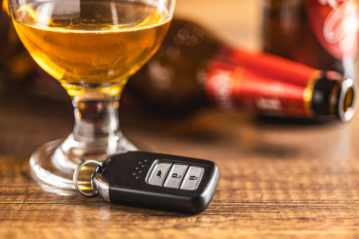 A car key sitting next to a glass of alcohol.